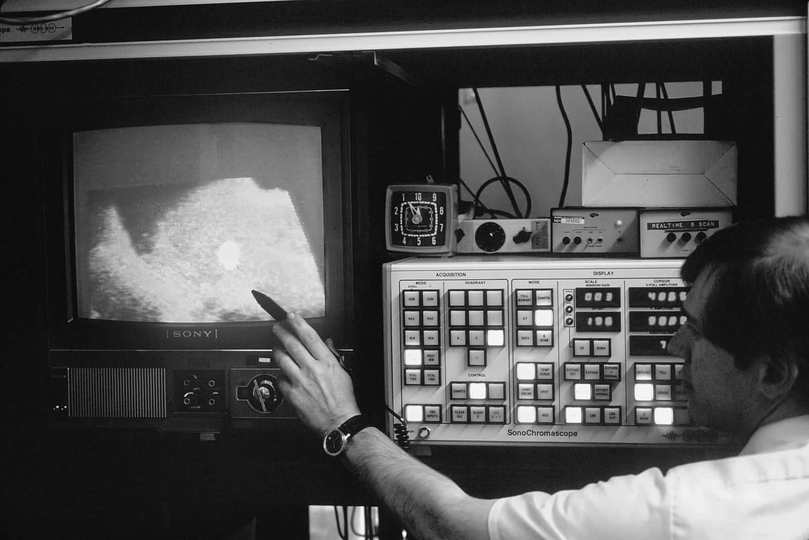 Ein Mann zeigt auf einen Monitor neben einem Steuerpult, Archivfoto